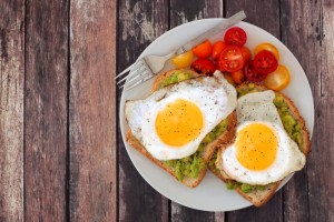 Healthy avocado, egg open sandwiches on a plate with colorful tomatoes against a rustic wood background