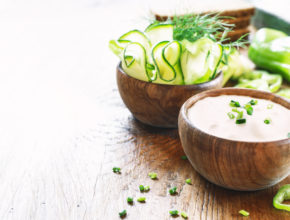 Tzatziki sauce in wooden bowl, with ingredients - cut cucumber, mint, dill on a dark wooden background with free text space. selective focus.