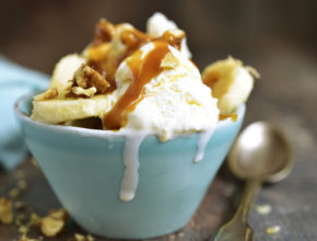 Vanilla ice cream with walnuts,banana and caramel in a blue bowl on a rustic wooden background.